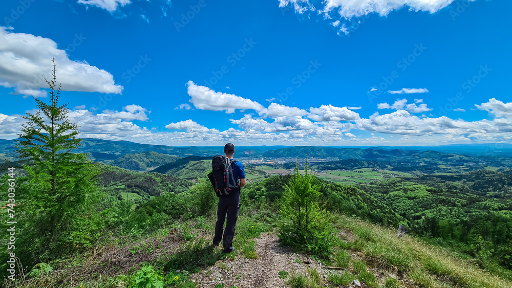 Hiker man on rock formation along idyllic hiking trail through lush green forest in Grazer Bergland, Prealps East of the Mur, Styria, Austria. Vibrant green leaves. Soft hills in alpine landscape