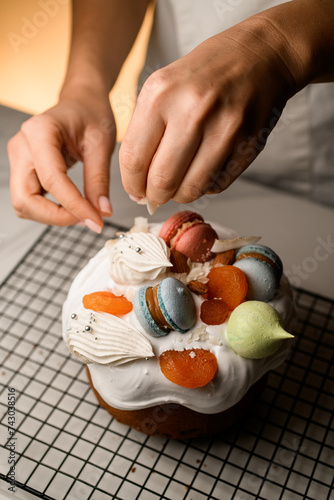 Baker decorates the Easter cake with colorful macaroons, dried apricots and meringue photo