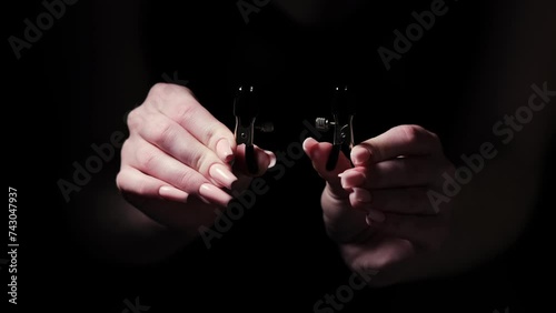 Two metal BDSM nipple clamps in female hands on a black background. Products for intimate stores, sex toys, adult gifts for couples
