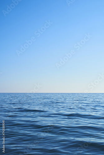 Blue water from the sea with a blue sky. Light comes from the right. Vertical format, also suitable as a poster or background. Free space for text, objects or other things.