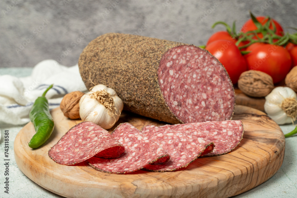 Peppered salami and slices on cutting board. Italian salami with pepper on gray background. Close up Peppered salami and slices on cutting board. Italian salami with pepper on gray background. Close up