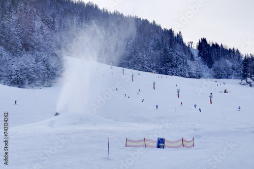 Snow gun making snow in Kranjska Gora, Slovenia, with skiers in the background on the slopes