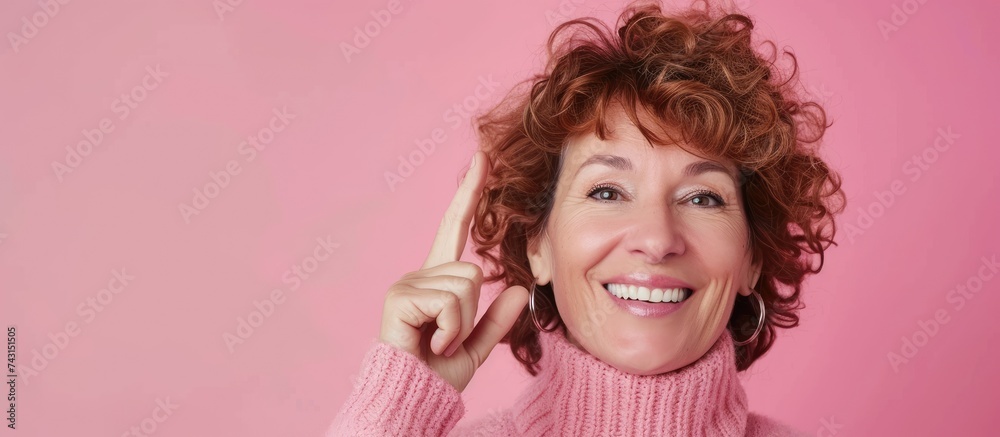 A middle-aged woman with curly hair wearing a pink turtleneck sweater is holding a toothbrush in her hand, smiling warmly in front of a pink background. She appears to be getting ready for her daily A middle-aged woman with curly hair wearing a pink turtleneck sweater is holding a toothbrush in her hand, smiling warmly in front of a pink background. She appears to be getting ready for her daily