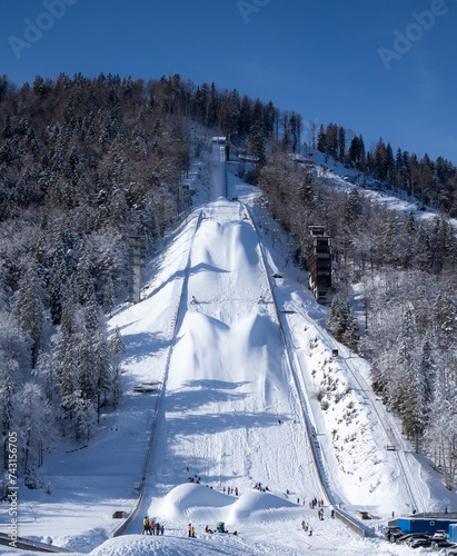 Giant Planica Ski Jump with Snow-Covered Slopes on a clear sunny winter day. People playing on snow at the bottom of the ski jump