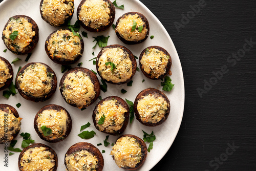 Homemade Garlic Parmesan-Stuffed Mushrooms on a plate on a black background, top view. Copy space.