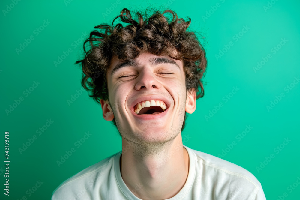 A man with his eyes closed and a twisted mouth trying to hold back laughter on a green background A man with his eyes closed and a twisted mouth trying to hold back laughter on a green background