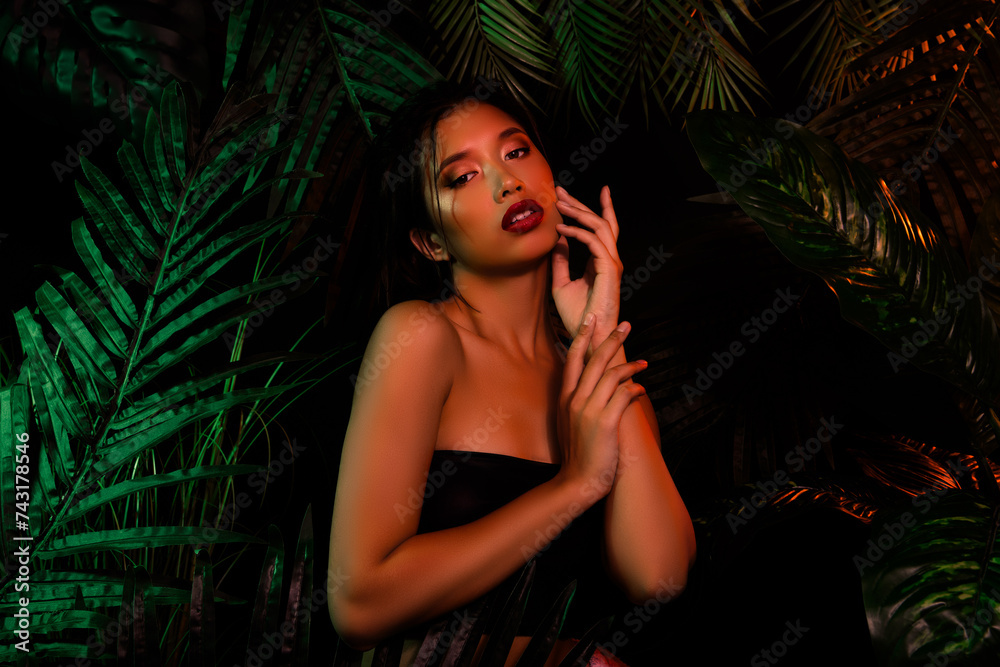 Photo of japanese asian girl touch her face hands over dark palm tree leaves Photo of japanese asian girl touch her face hands over dark palm tree leaves