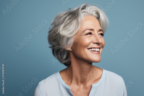 smiling senior woman with short grey hair looking away over blue background