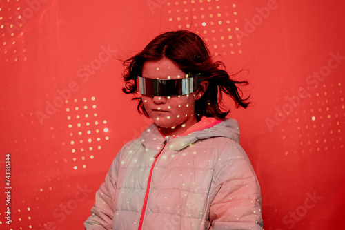 Girl with a serious expression, sporting reflective futuristic glasses and a white puffer jacket, against a dotted red backdrop photo