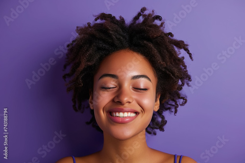 A woman with her eyes closed and a smile on a purple background