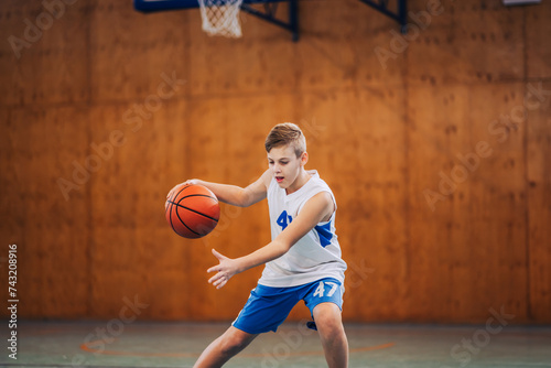 Dynamic portrait of junior basketball player dribbling a ball on court. © Zamrznuti tonovi