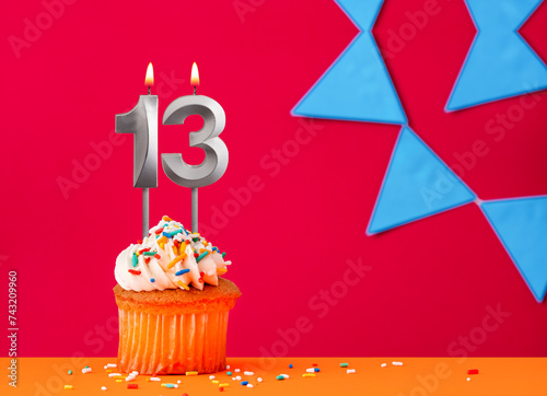 Birthday cupcake with candle number 13 on a red background with blue pennants