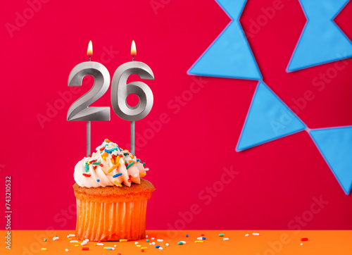 Number 26 candle with birthday cupcake on a red background with blue pennants