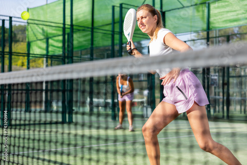 Sporty european woman padel tennis player trains on the outdoor court using a racket to hit the ball