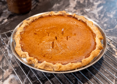Home made and fresh baked pumpkin pie, waiting to be eaten as it sits on a metal cooling rack on the kitchen counter.