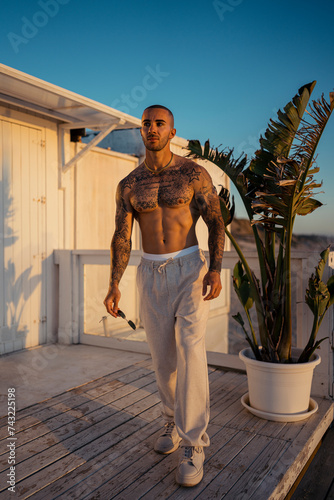 Chico joven musculado y tatuado posando en la playa sin camiseta al atardecer © MiguelAngelJunquera