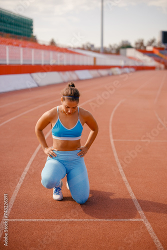 Active female athlete kneeling on the tartan racetrack at the stadium