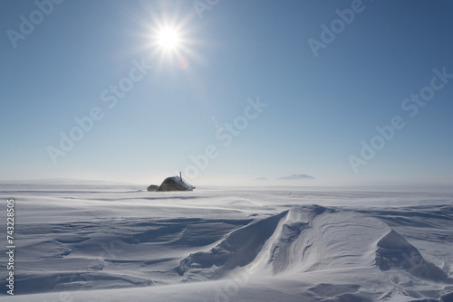 Winter arctic landscape. View of a small house in the snowy tundra. Cloudless sunny cold frosty weather. Abandoned building in the Arctic. Chukotka, Siberia, the Far North of Russia. Polar region.