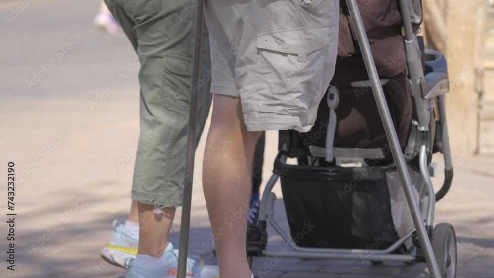 This video shows a close up view of a one legged man standing next to a baby stroller. This video shows a close up view of a one legged man standing next to a baby stroller.