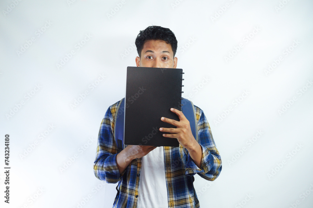 Shocked young Asian students with backpacks covering half faces with books isolated on white background. Education in high school university college concept