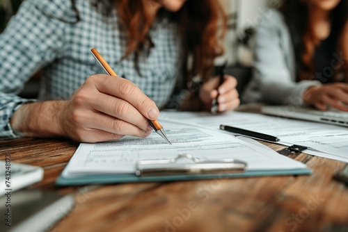 Two people sit at a table, diligently working with papers and a pen to complete financial paperwork.