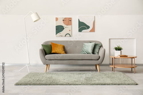 Interior of light living room with stylish sofa, pictures and table
