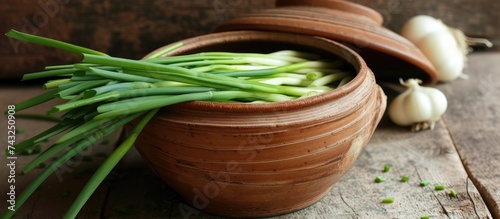 A clay pot filled with freshly harvested green onions and garlic, showcasing a bounty of fresh produce ready for culinary use.