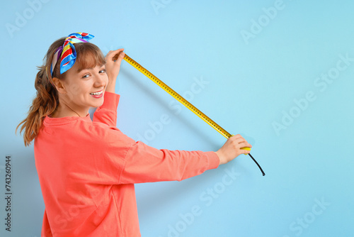Young woman with tape measure on blue background. Repair concept