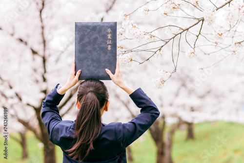 満開の桜の下で卒業証書を頭の上に載せる高校生・女子高生（卒業生・卒業・卒業式） 