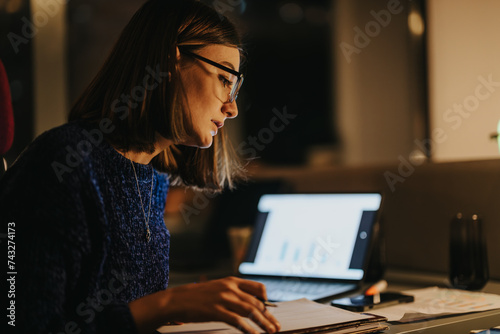 Canvas-taulu Female business executive analyzing graphs on a laptop in a modern office setting, showcasing dedication and concentration
