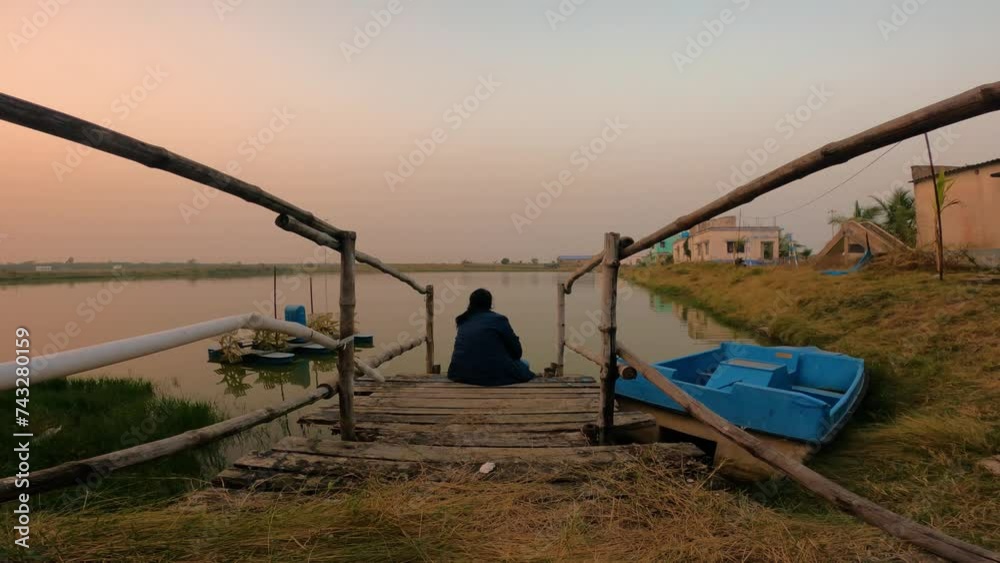 An young solo traveler enjoying sunset sitting on bamboo stair beside a pond at Henry Island, West Bengal. An young solo traveler enjoying sunset sitting on bamboo stair beside a pond at Henry Island, West Bengal.