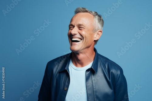 Handsome mature man laughing and looking away while standing against blue background