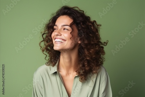 Portrait of a beautiful young woman with curly hair smiling against green background