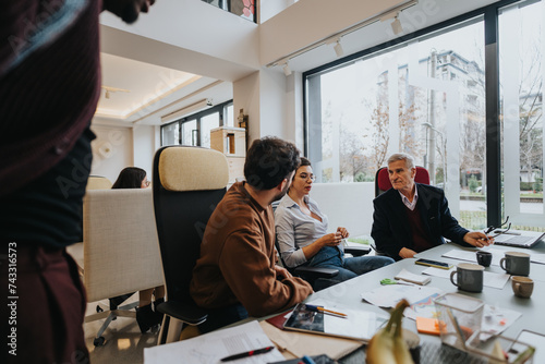 A different aged group of employees actively participating in a business meeting in a well-lit contemporary office setting, exchanging ideas and strategies.