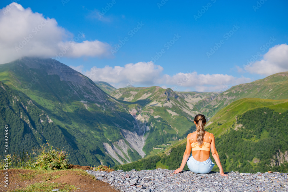Young Woman in Blue Suit Admiring Gorgeous Mountain Landscape with Lush Green Trees and Blue Sky