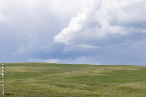 Scenic nature landscape of a hill covered in green grass with moody and dramatic storm clouds in the sky above it.