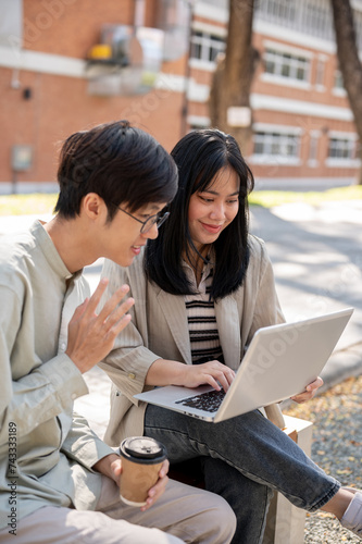 Two smart Asian students are collaborating on a project while sitting together in the park.