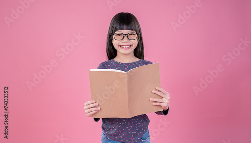 Portrait of little cute asian toddler nerd glasses girl reading book isolated on pink background, Education knowledgement. Nerd reader girl studying, home school and back to school concept © paulaphoto