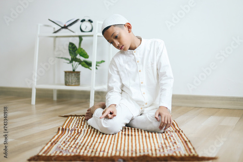 Young moslem boy praying on prayer mat and doing tashahhud, last movement on salat procedure photo