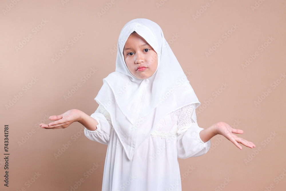 Asian muslim little girl with hijab shrugging her shoulder showing don't know and clueless gesture Asian muslim little girl with hijab shrugging her shoulder showing don't know and clueless gesture