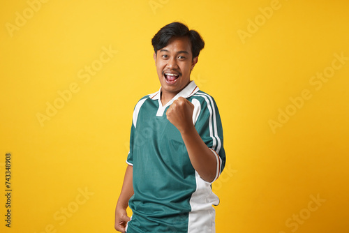 Yes, Achievement Concept. Excited young asian man cheering and screaming, celebrating victory. Emotional overwhelmed guy yelling and shaking clenched fists, isolated over orange background