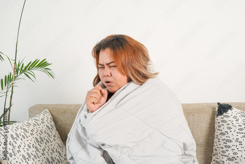 An Asian woman feeling unhealthy with a headache and cough sleeps under the blanket. She coughs all the time. An Asian woman feeling unhealthy with a headache and cough sleeps under the blanket. She coughs all the time.