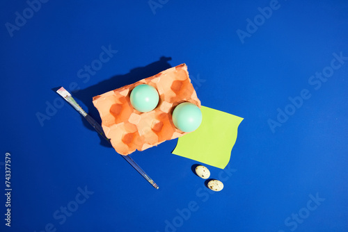 Coral egg carton containing blue Easter eggs decorated with a paintbrush and a note paper on the blue background. Easter, principal festival of the Christian church photo