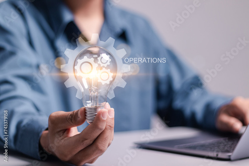 Operational concept. Businessman holding light bulb with operation icon for productivity with excellence process. Industrial management in efficiency and efficient process. photo