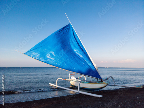 Traditional fishermen boat with a sail at the black sand beach shore in Amed  village, karangasem district, Bali photo