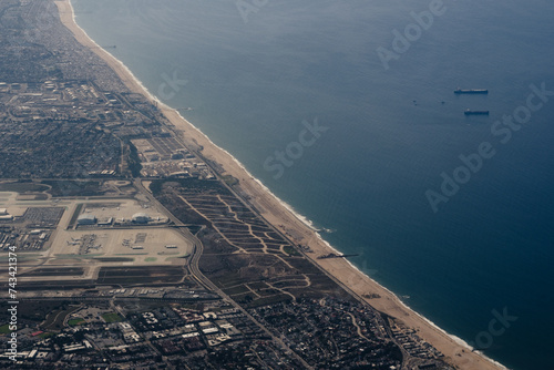 Aerial view of the shoreline of Los Angeles, with a view of the runways of Los Angeles International Airport (LAX) and large freight ships off the coast.