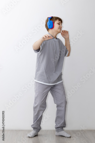 teenage boy in a grey suit is dancing merrily to music with headphones