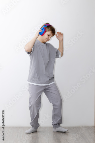 teenage boy in a gray tracksuit is dancing to the music with headphones, his head tilted