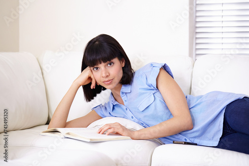 Portrait, couch and woman reading book in home, relax and learning in living room in the morning. Sofa, young student and person with novel for studying literature in lounge in apartment in Spain