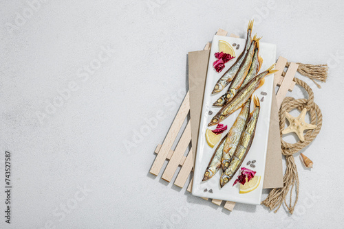 Smoked smelt with fresh lemon and herbs. Salted fish with marine decor. Trendy dish, sea rope photo